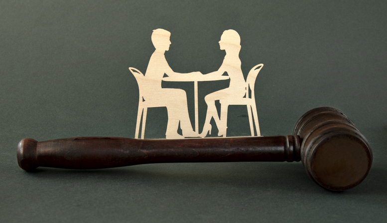 Wooden figurines of a man and a woman sitting at a table against the background of a judge's hammer. Family law. divorce mediation